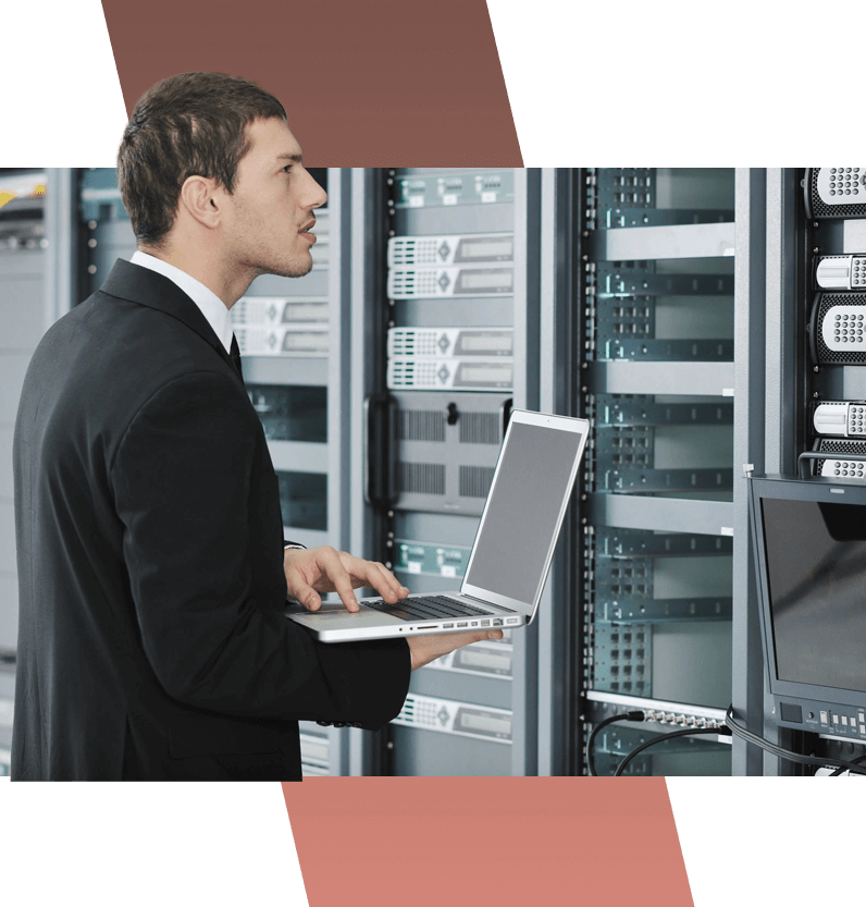 A man in black suit holding laptop near server racks.